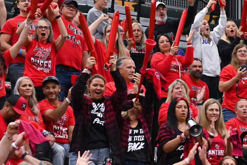 Crowd at a STUNT game. Dressed in red and black, cheering and using bang stick noise makers.